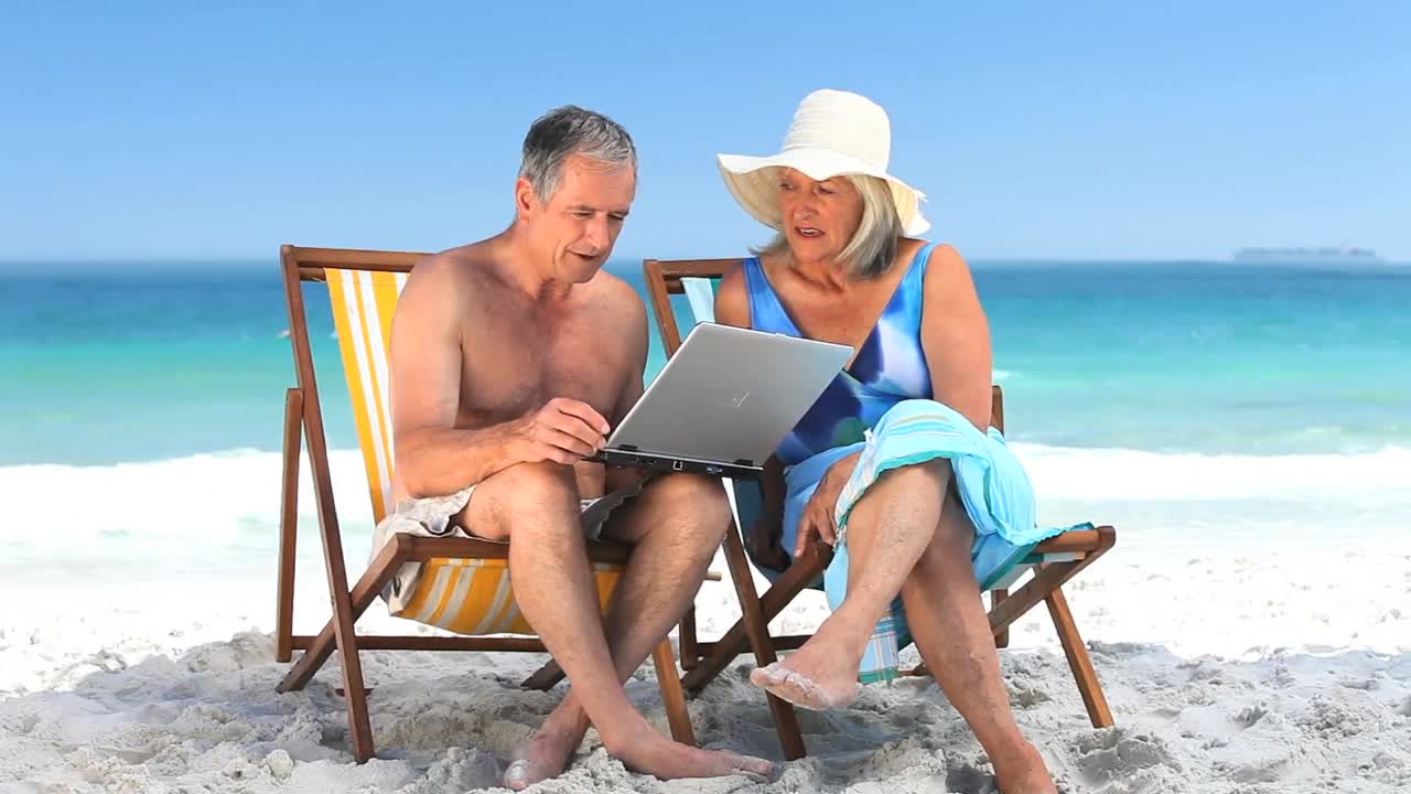 pareja de ancianos usando una computadora portátil sentada en sillas de playa