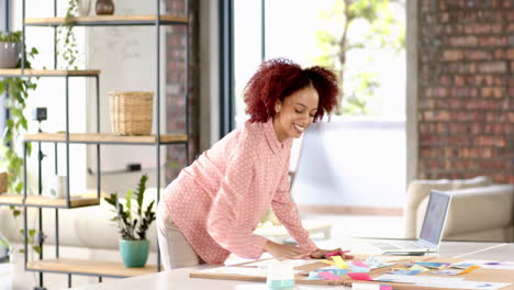 smiling woman brainstorming ideas, using sticky notes and laptop in creative office