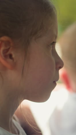 cute little girl with ponytail sits with brother near motorboat window closeup. sister turns head to look at toddler boy during river cruise