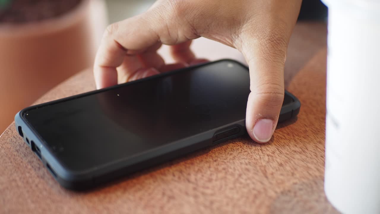 Person using smartphone at a wooden table in a cafe