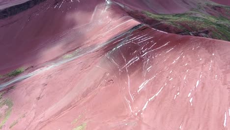 Drone-view-in-Peru-flying-over-red-valley-in-Cuzco,-showing-red-colored-mountains-surrounded-by-snowed-mountains-in-the-horizon