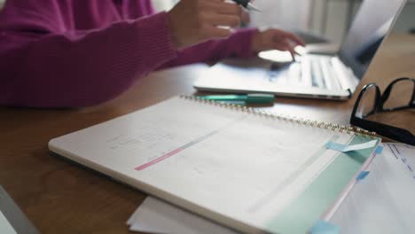 mujer irreconocible trabajando en la computadora y tomando notas en casa