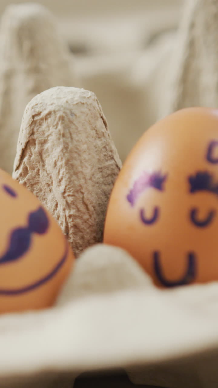 Video of close up of two brown eggs with drawn faces in egg carton background