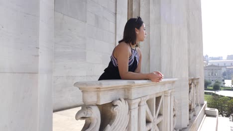 Shot-of-a-young-asian-woman-who-stands-on-a-balcony-of-an-old-marble-building-in-athen