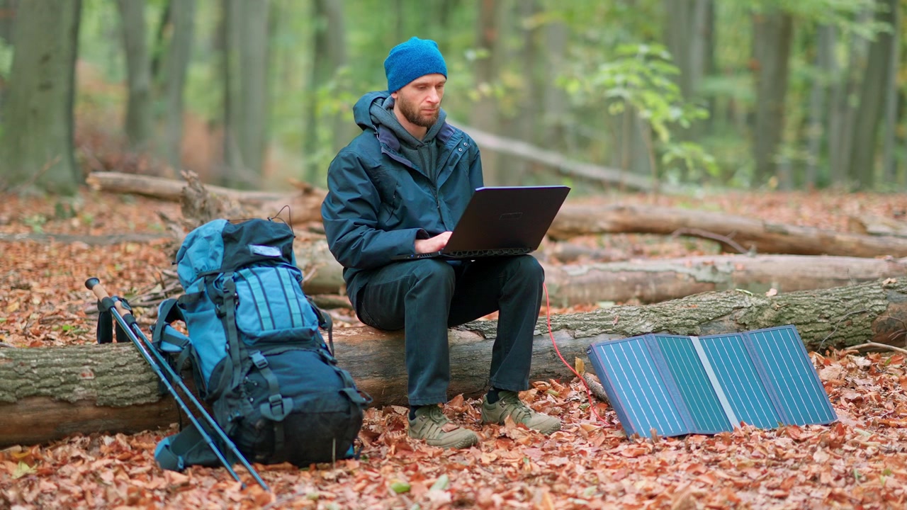 Uomo che lavora al laptop in una foresta autunnale con un pannello solare portatile