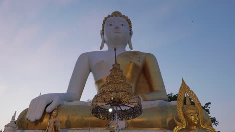 4k cinematic religious travel footage of a giant statue of buddha at the temple of wat phrathat doi kham in chiang mai, northern thailand during a beautiful sunset on top of a mountain