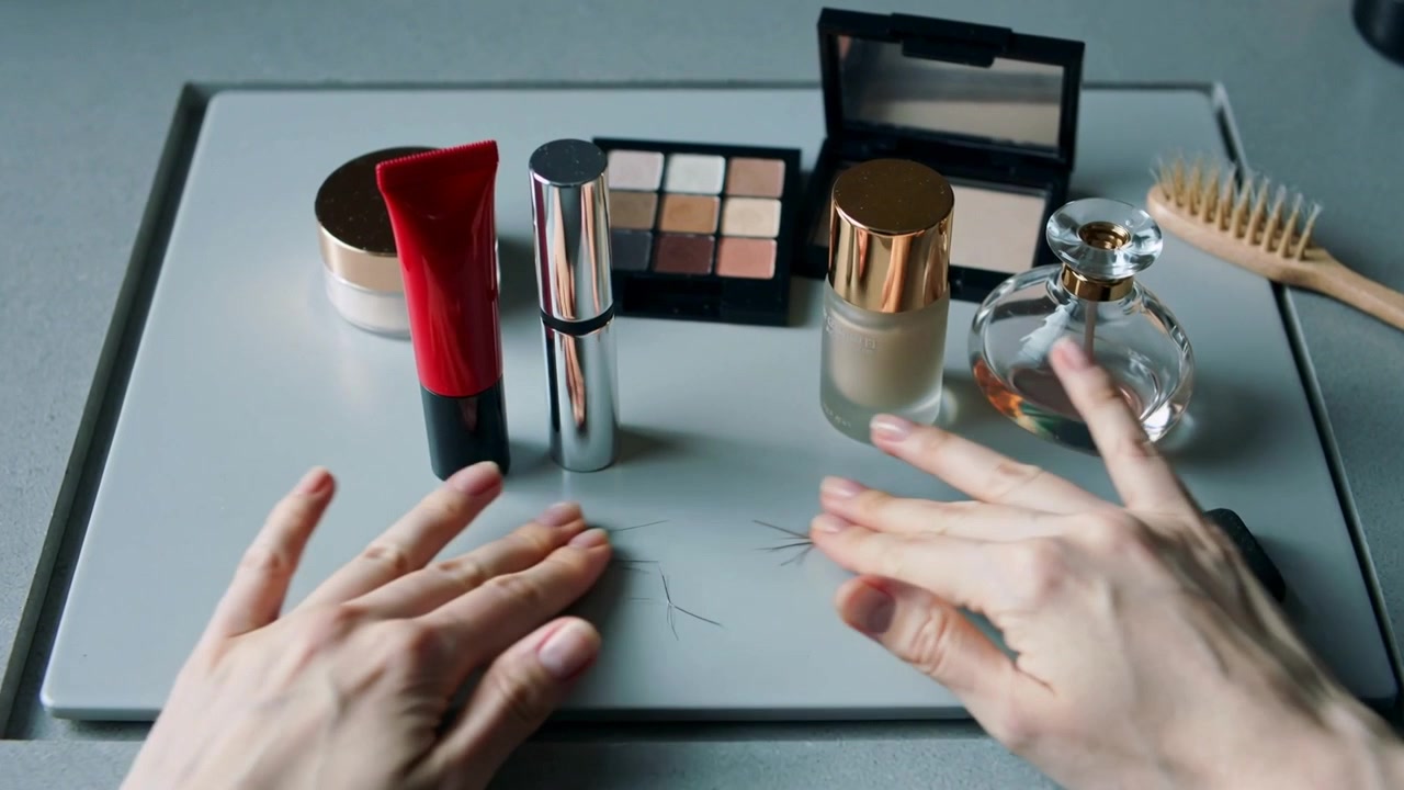 Entering frame pair of hands grabbing red tube and silver cylinder on vanity tray, preparing makeup