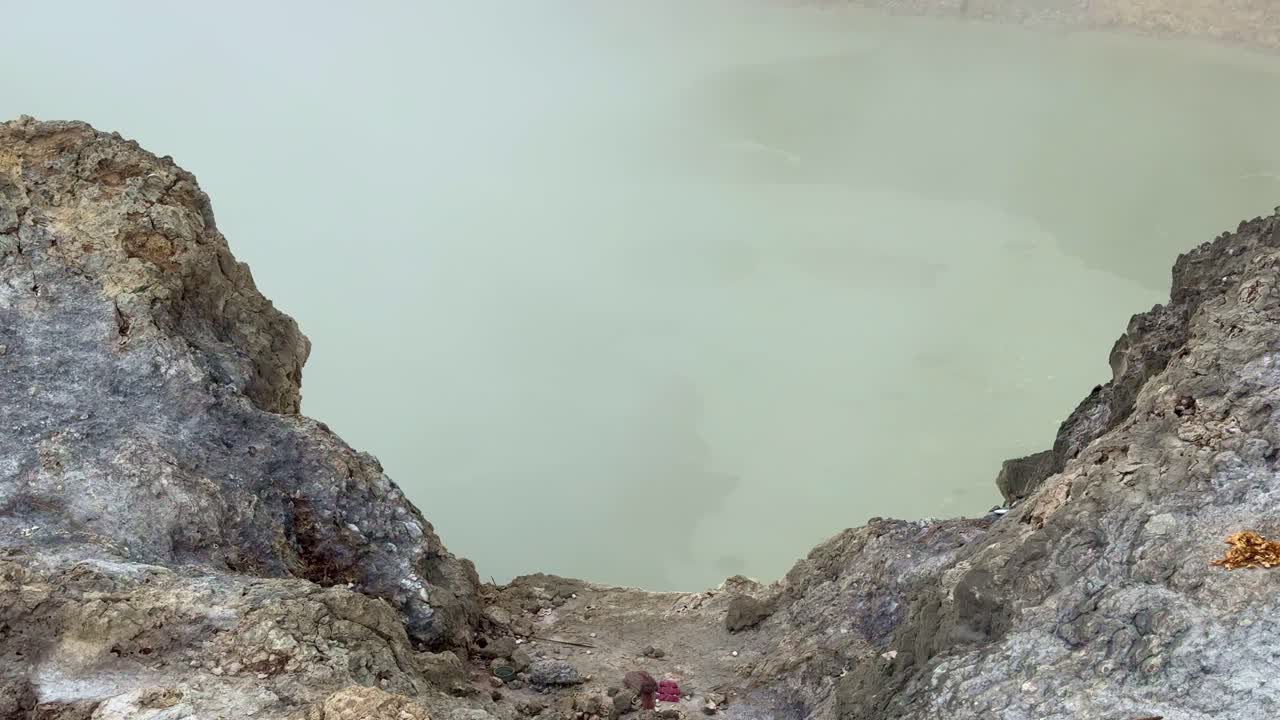 Pozza di zolfo fumante con acqua calda gorgogliante in un paesaggio vulcanico. Fenomeno geotermico naturale che produce fumo e trame ricche di minerali intorno al cratere