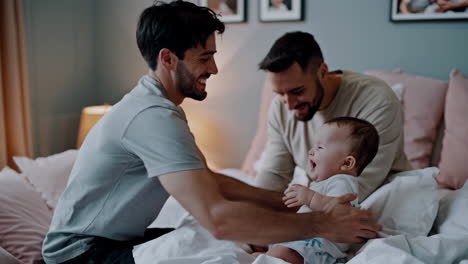 two dads playing and bonding with their happy baby in bed