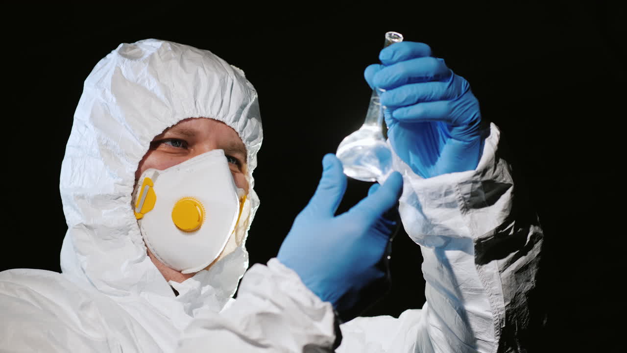 보호복과 호흡보호구를 착용한 남자가 플라스크를 검사하고 있다 3