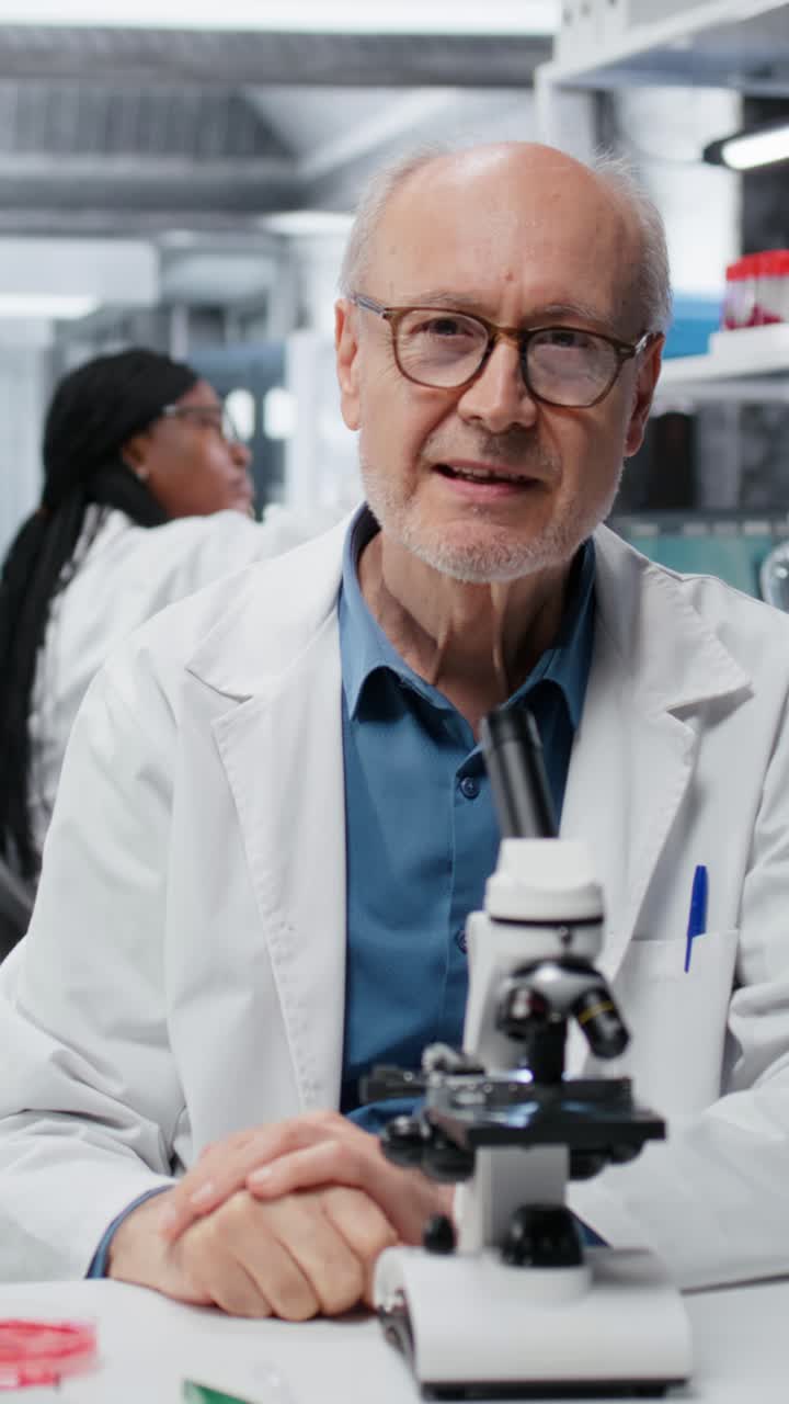 Vídeo vertical. Un profesional de laboratorio de edad avanzada, con un toque alegre, investiga las propiedades de un polímero líquido azul