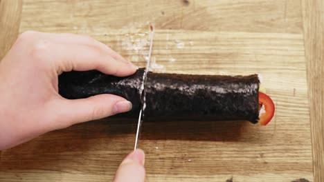 woman cutting sushi into pieces on table in kitchen