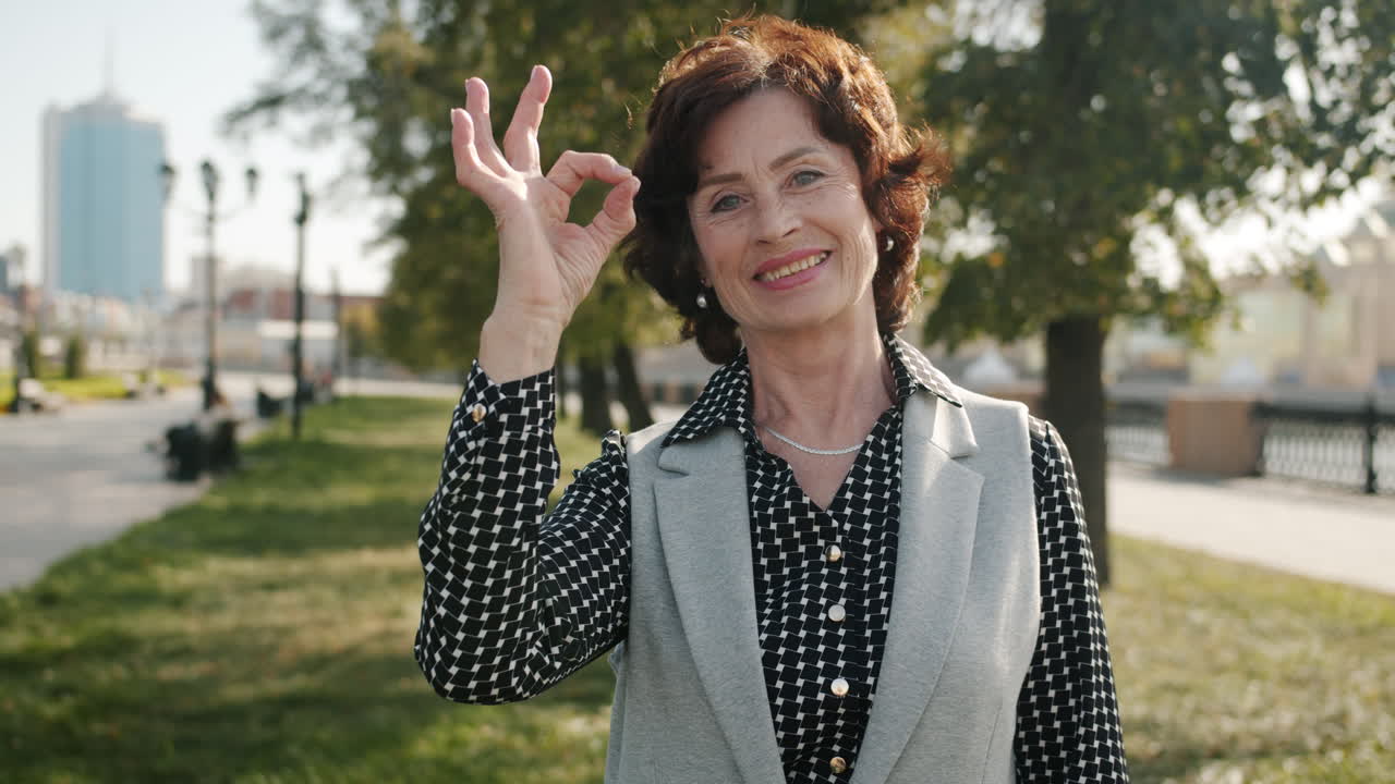 Smiling Older Woman Giving the OK Sign in a Park