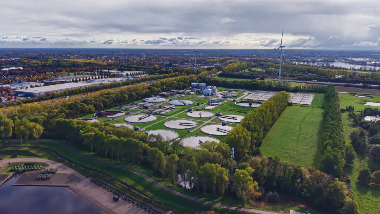 Water treatment facility operating with renewable energy near a tranquil lake and surrounded by green trees during a bright cloudy day