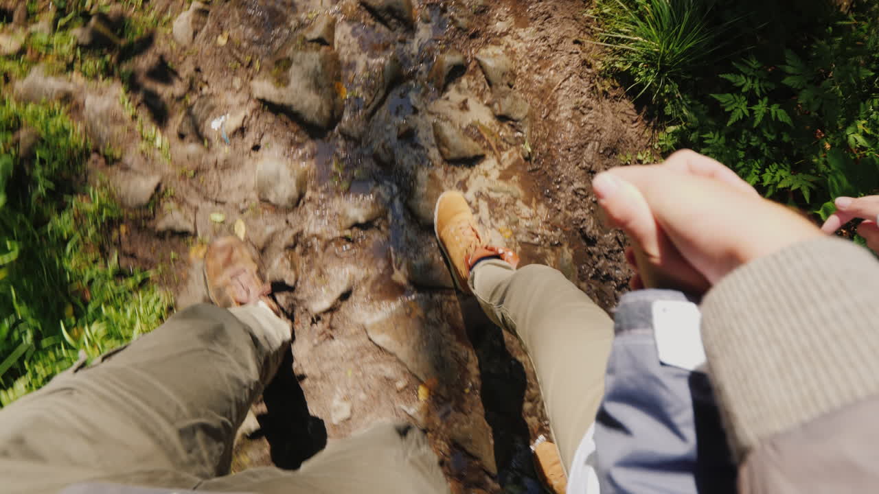 두 명의 관광객이 손을 잡고 숲속의 미끄러운 돌길을 걷는다.