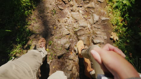 a couple of tourists hold hands and walk on a slippery stony path in the forest only the legs are vi