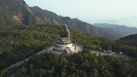 aerial drone view of the hong kong buddha statue atop a hill, surrounded by greenery and scenic mountain ranges