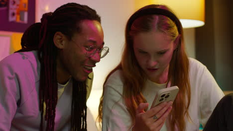 two young people laughing together while looking at a phone