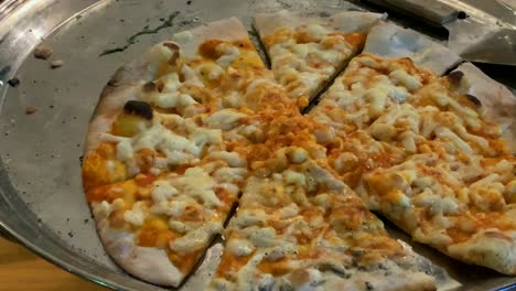 pizza en pedazos o rebanadas en una bandeja de metal sobre un fondo de mesa de madera, con una fina corteza de pastel, primer plano. 4k
