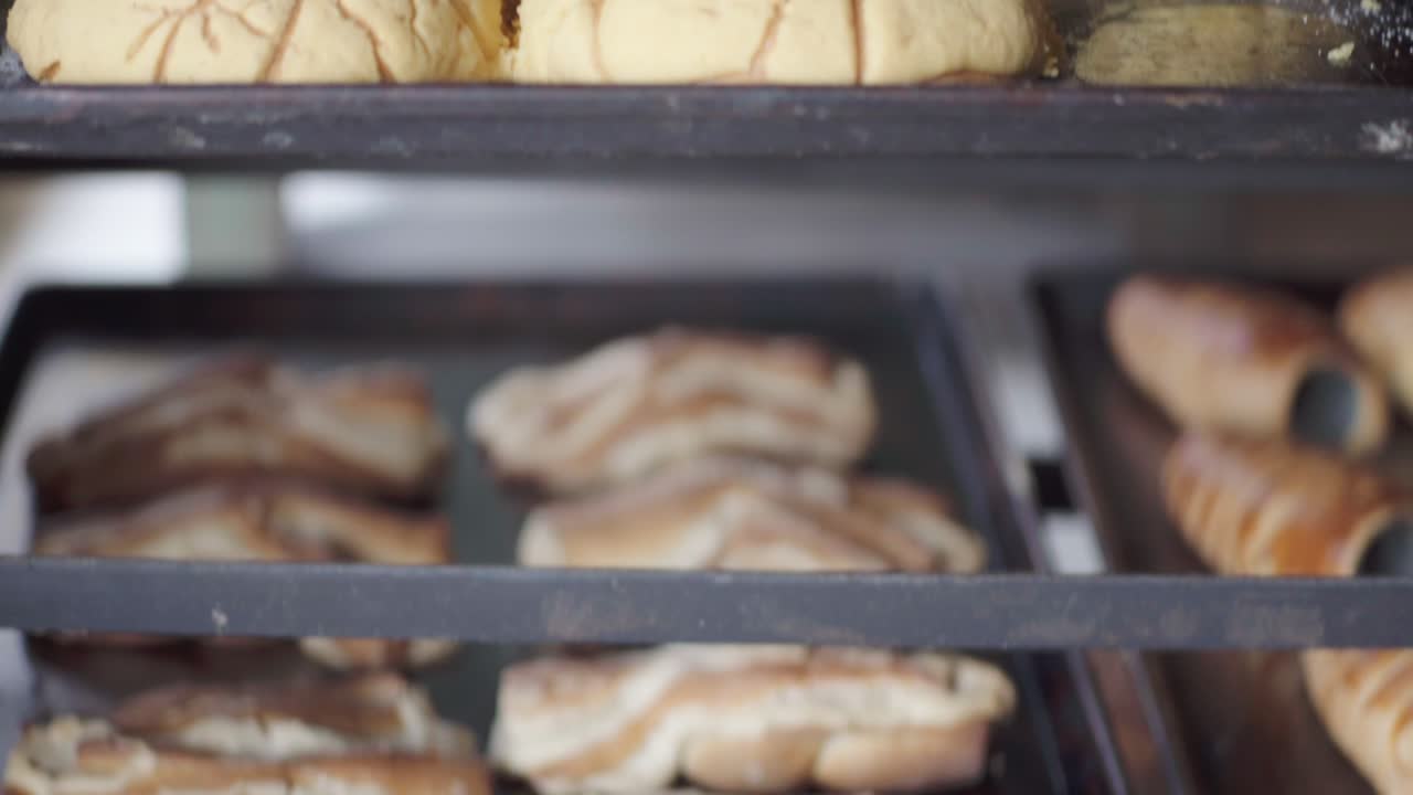 Close-up of multiple trays filled with assorted baked pastries cooling on racks inside a bakery.