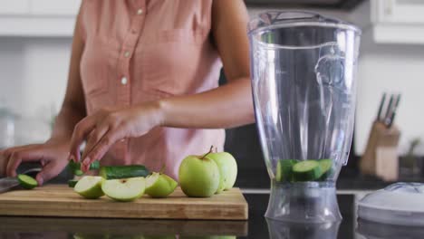 Mid-section-of-african-american-woman-chopping-vegetables-and-putting-it-in-glass-jar-at-home