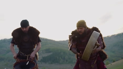 folk musicians in ethnic clothes play drums in valley