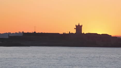 Sommerlicher-Blick-Auf-Die-Ersten-Strahlen-Der-Sonne-Beleuchten-Die-Festung-Von-Saint-Julian-Am-Carcavelos-strand,-Der-Von-Einem-Orangefarbenen-Himmel-Bedeckt-Ist