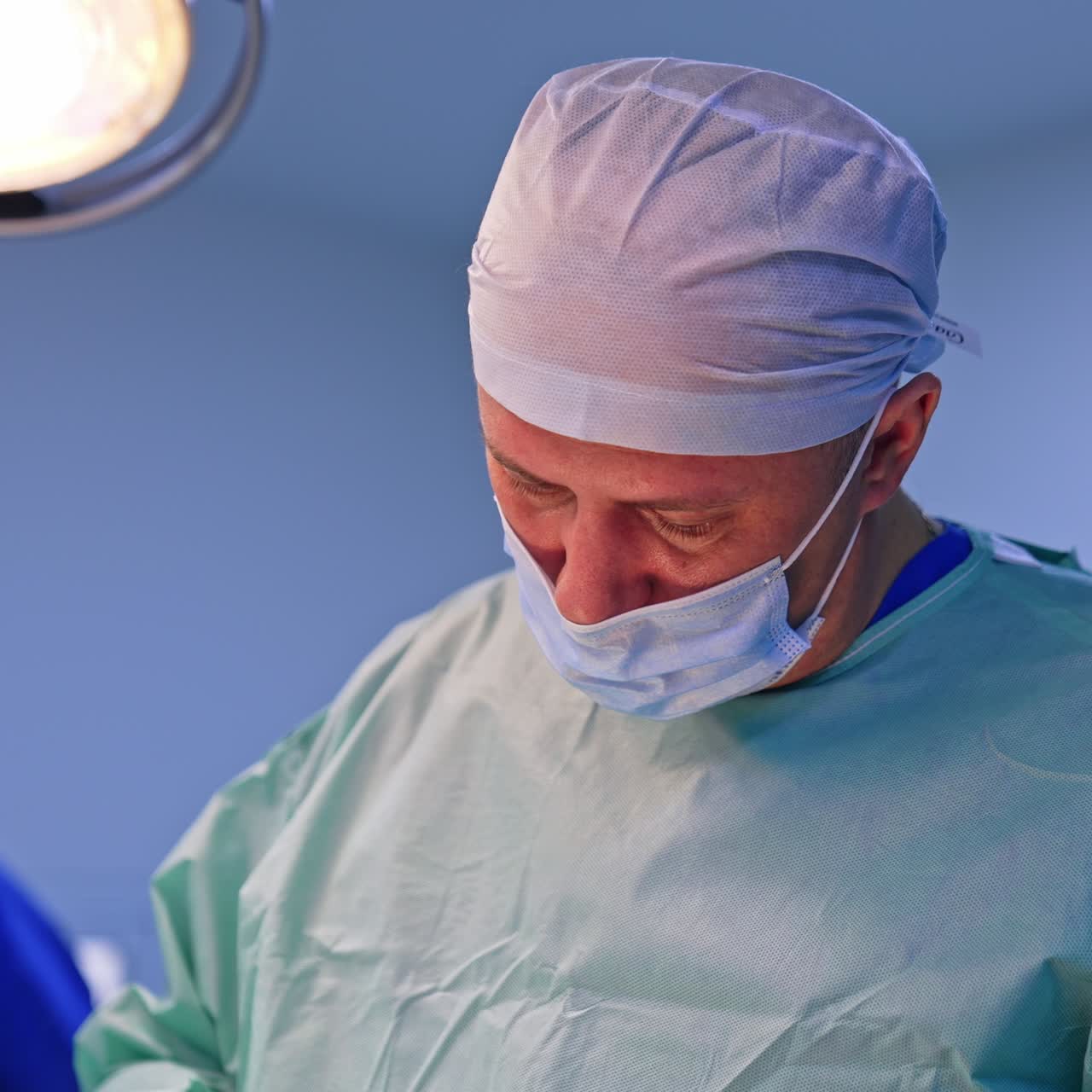 Confident experienced surgeon working at operation. Portrait of a focused professional looking down at patient. Close up