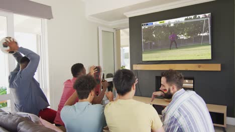 video of diverse friends sitting on sofa and watching football on television at home