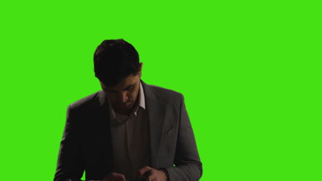 businessman making call on mobile phone walking into frame against green screen background with low key lighting