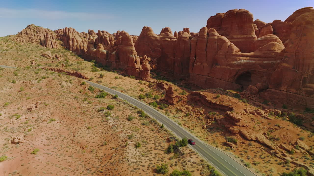 Cars moving by the motorway locating along the odd-shaped orange rocks. Wonderful canyons of Arches national park, Utah, USA.