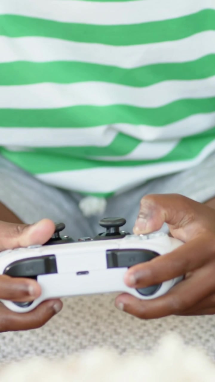 Vertical video: Picking up white controller, boy in green shirt playing game on couch with father