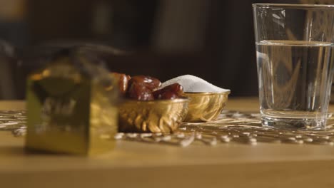 tazón de dátiles con vaso de agua y cajas de regalo sobre la mesa en un hogar musulmán celebrando el eid 3