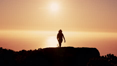 silhouette of a hiker on a cliff overlooking the ocean at sunset