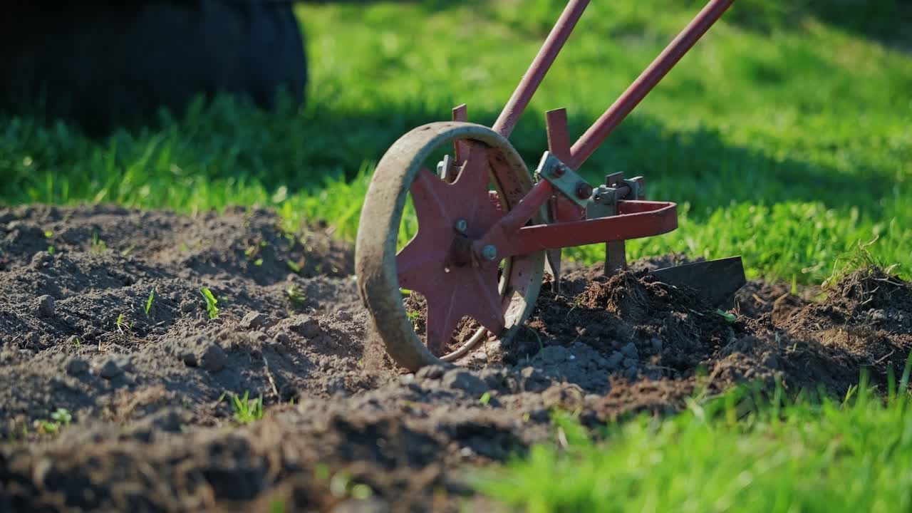 Slow motion nærbillede af en manuel kultivator, der løfter og vender jorden i sollys