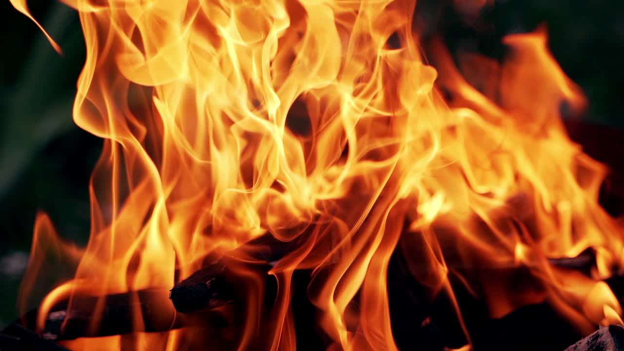 Detailed motion of orange flame on the black background. Close-up bright fantastic flame on firewoods outdoors.