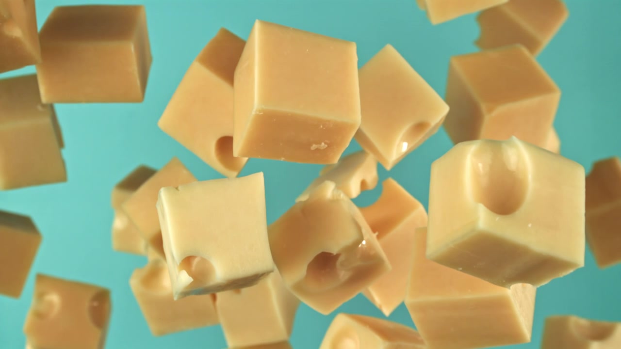 Ralenti de cubes de fromage troués tombant sur un fond bleu
