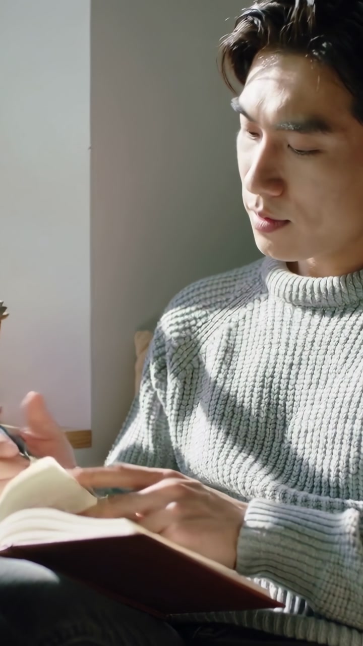 Vertical video: Turning page, Asian man in gray sweater writing notes in notebook with pen