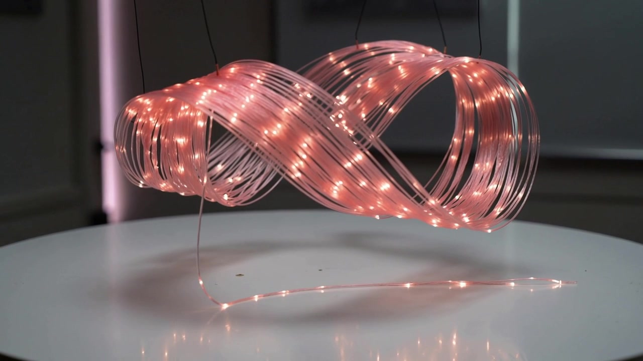 Reacting to power pulse, suspended LED ribbon sculpture morphing above pedestal, with pink LEDs
