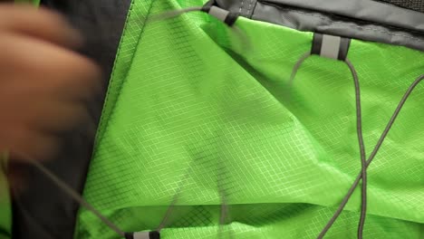 a stationary footage of a green backpack with elastic laces being pulled to get fastened by the toggle in preparation for the journey