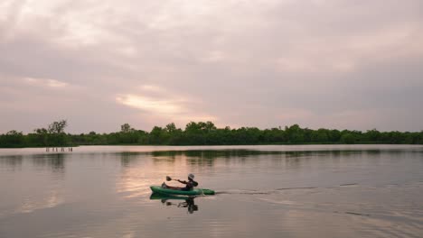 lone kayaker paddling across serene lake at sunset