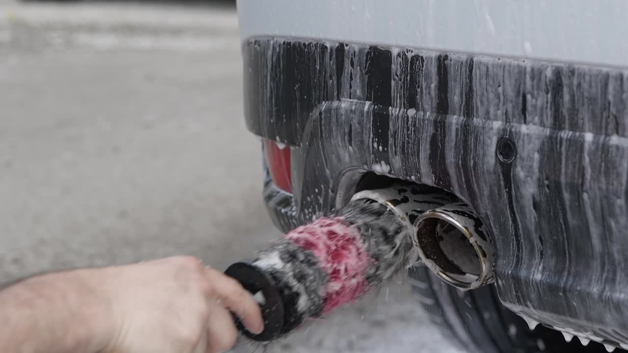 Close up cleaning twin dual exhaust with snow foam and detailing brush
