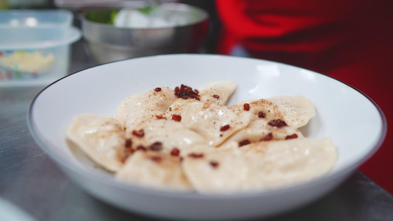 Chef's Hand Topping Freshly Cooked Dumplings with Bacon Bits and Pepper