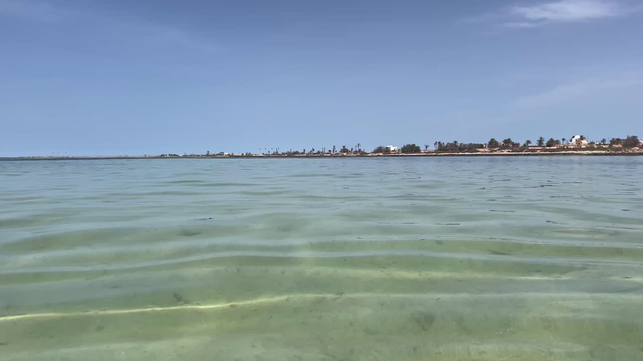 Calm waves gently lap against the shore as the sun shines brightly on the tranquil beach. Soft sand meets calm water, creating a perfect spot for relaxation and enjoyment