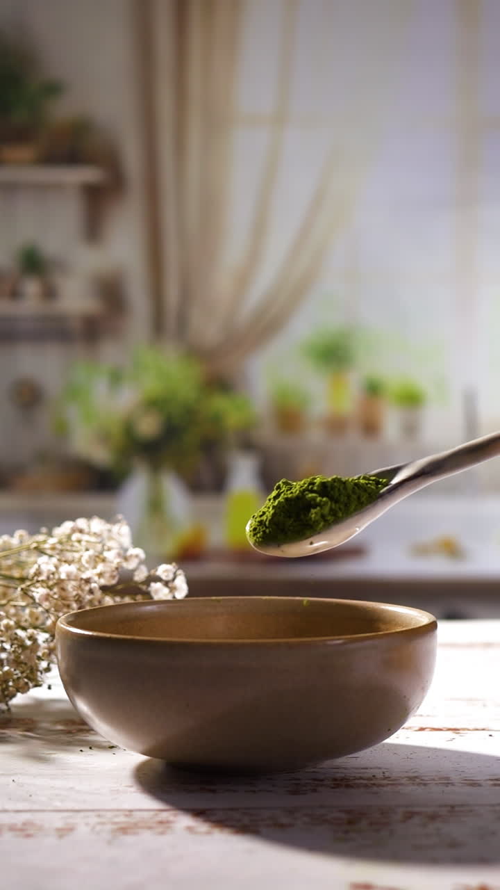 Slow-motion close-up of vibrant green matcha or vitamin, chlorella, spirulina powder falling from spoon into wooden bowl, emphasizing natural ingredients, antioxidants, plant-based health benefits.