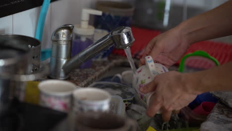 a man washes a cup under a tap in a sink full of dirty dishes