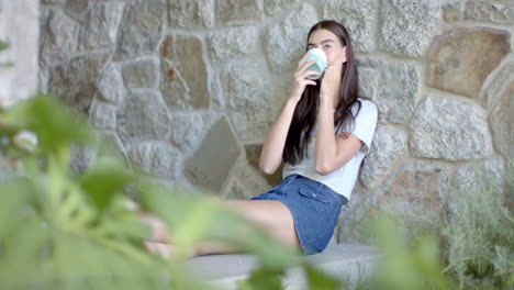 teenage caucasian girl with long brown hair enjoys a drink on a stone ledge at home with copy space