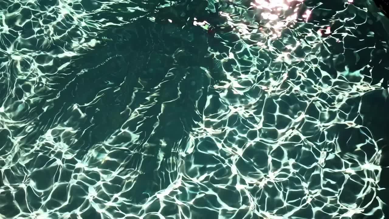 Top-down video shot of sunlight creating shimmering patterns on a swimming pool's surface