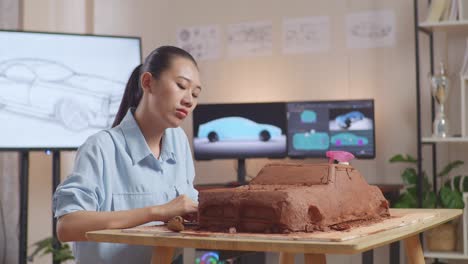 woman sculpting a clay model of a car in a home office