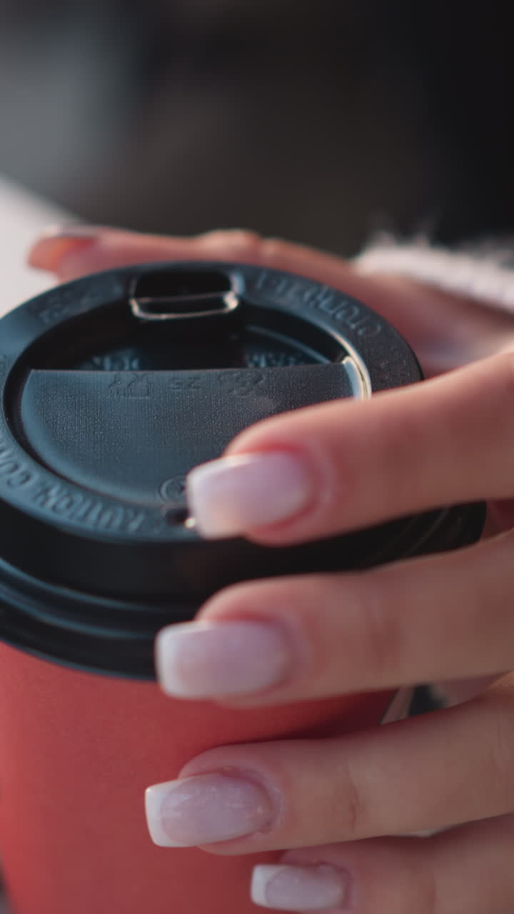primer plano de la mano de una mujer girando suavemente una taza de café cerca de una computadora portátil, centrándose en sus dedos manicurados contra un fondo borroso del teclado